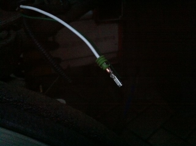 A white wire with a green seal and a crimped metal terminal on its end, in the dark behind the wheel
