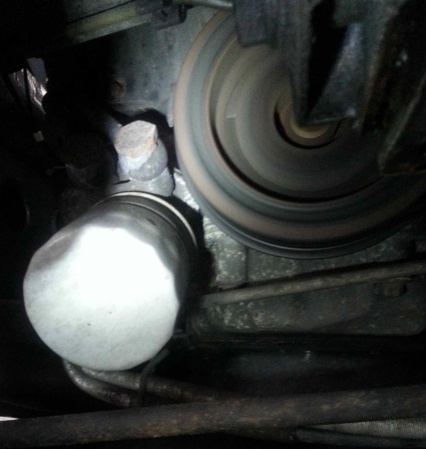 A blurred spinning crank pulley next to an oil filter, seen from below