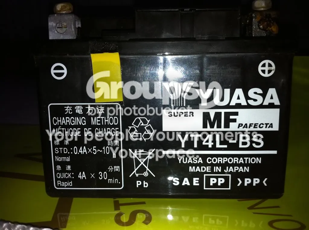 Close-up of the old battery label reading Yuasa YT4L-BS, with corroded terminals