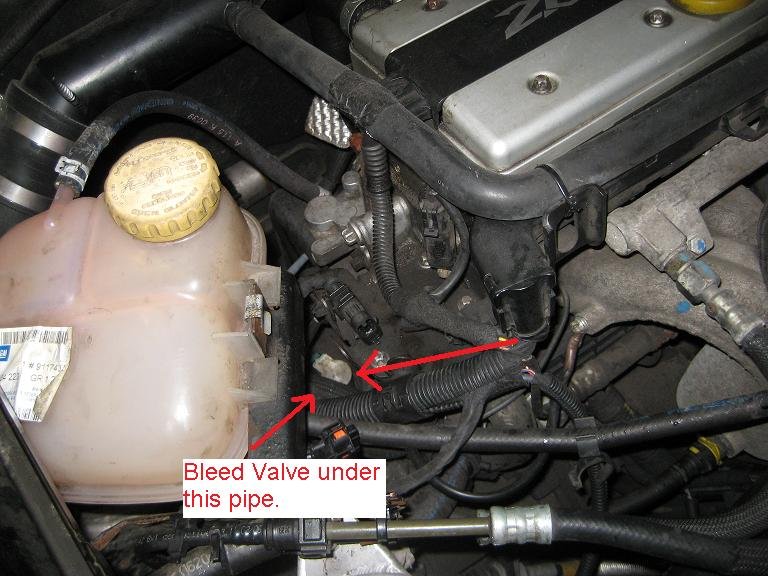 A Turbo engine bay with the coolant expansion tank at left and a red arrow pointing to the clutch bleed valve under a black pipe