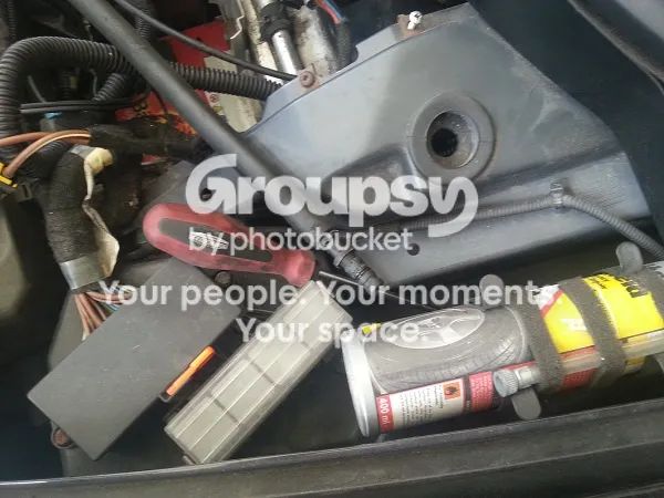 The engine bay near the wiper motor and fuse box, with a screwdriver and a can of spray lying on the shelf