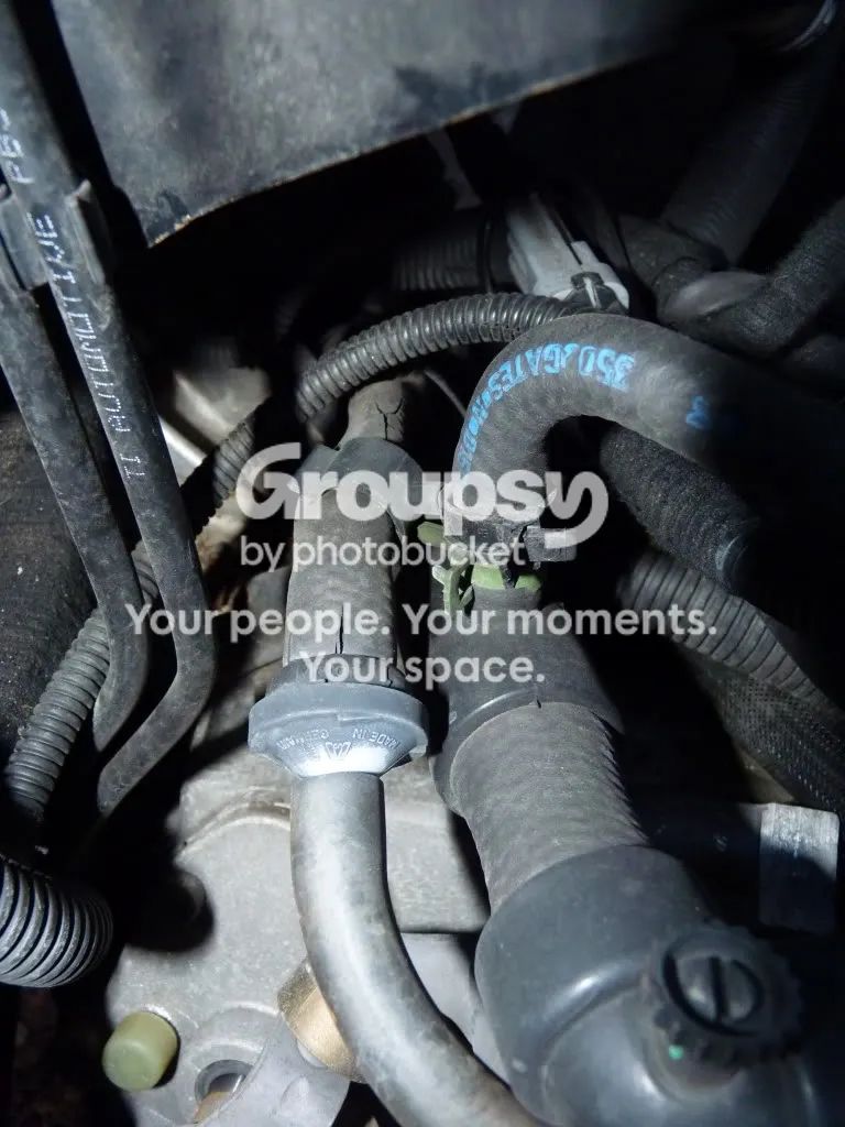 The engine bay near the manifold with a grey fitting and two black hoses and a blue-lettered hose