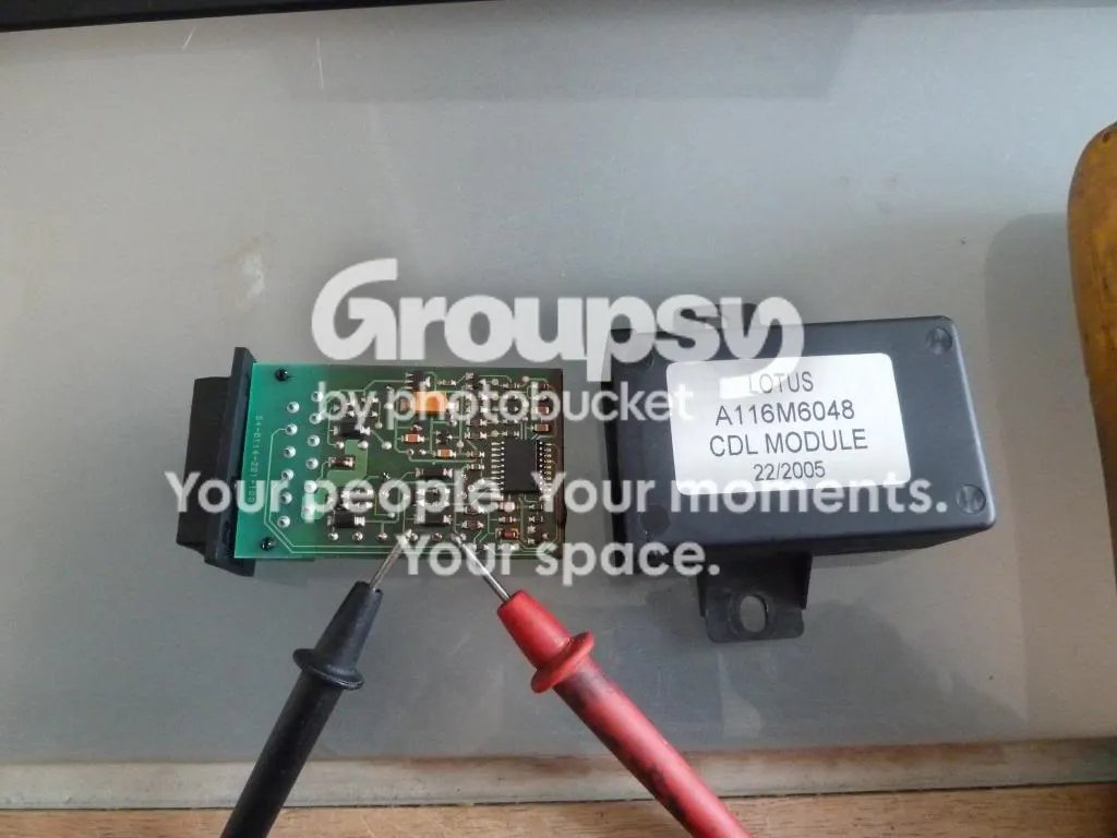 The CDL module circuit board with multimeter probes on its pads beside the black case