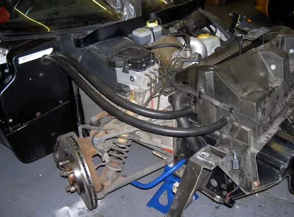 An engine bay seen from the side with two black hoses running along the sill toward the front of the car