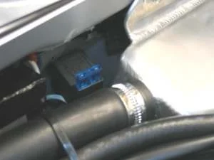 A relay with a blue fuse visible, fitted beside a silver tank and a black hose