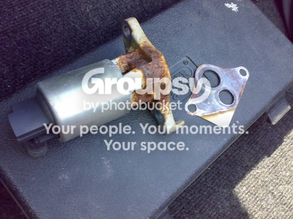 The old EGR valve, rusty at the bracket, lying next to its metal gasket