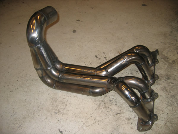 A stainless steel 4-1 exhaust header with four long primary pipes sweeping into a collector with a bend