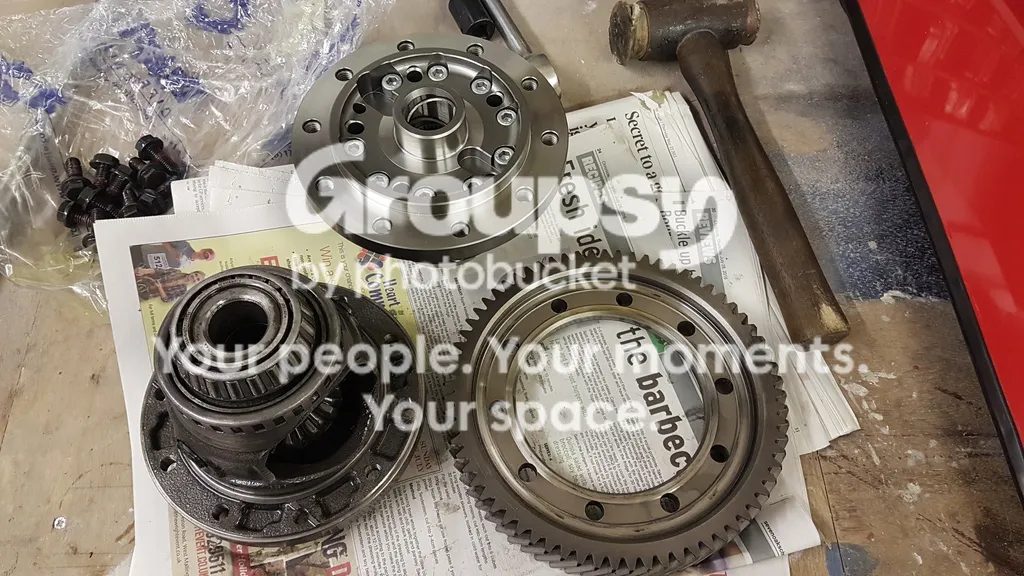 The old diff, the new limited-slip diff, the crown ring and a bag of bolts on newspaper, with a mallet
