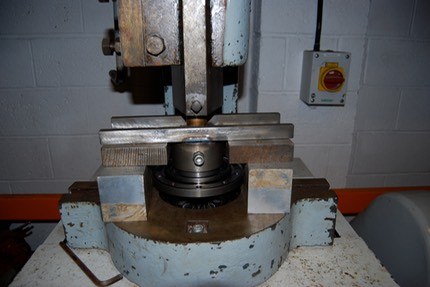 A diff with its bearing sat in a hydraulic press with a plate across the top