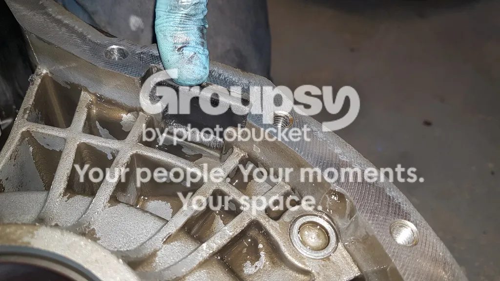 A gloved finger pointing at the magnet position in the gearbox case