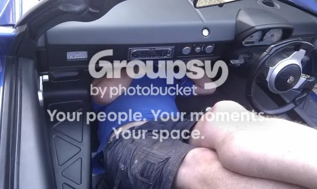 A person lying in the driver's footwell of a blue VX220 with their head up under the dash