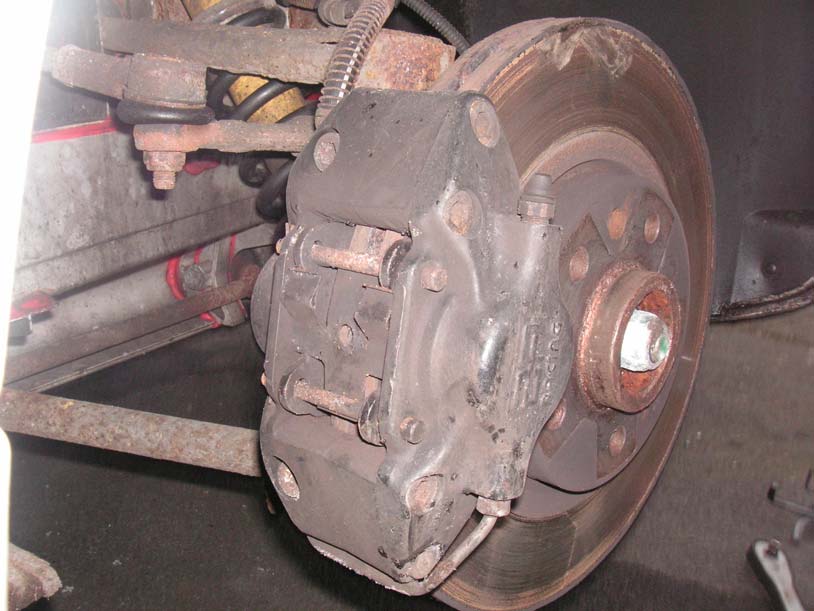 A front brake caliper on the hub with the hub nut visible and the disc behind it