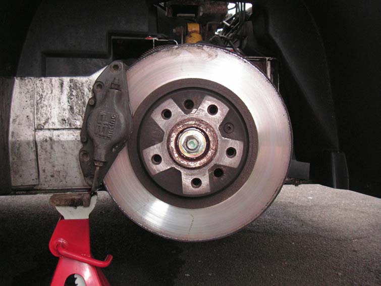 A bare brake disc on the hub with the caliper moved to one side and the car resting on an axle stand