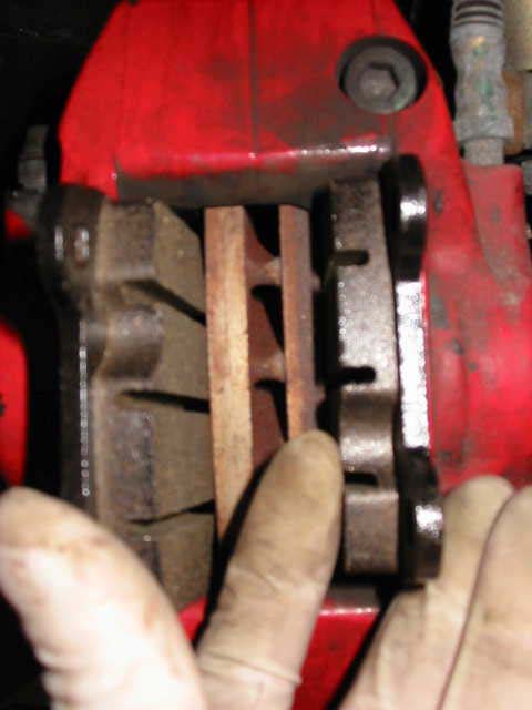 A hand sliding a pad into a red front caliper, next to the disc