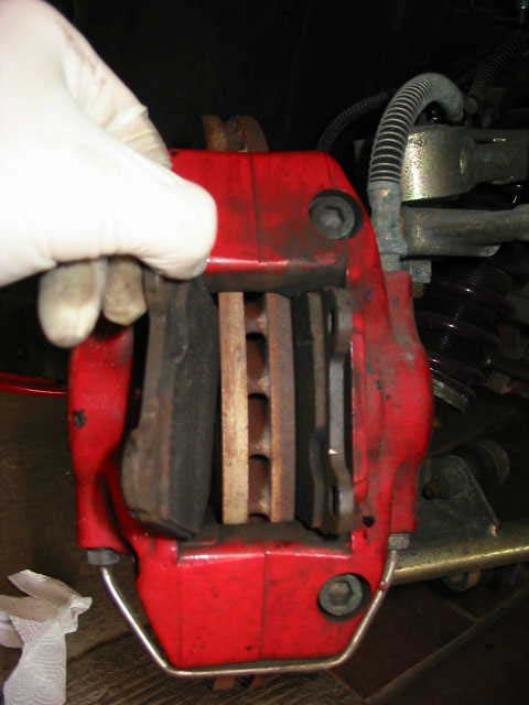 A red front caliper with one pad slid partly out and the disc between the pads