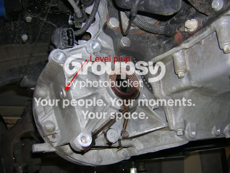 Underside view of the gearbox casing with a red arrow marked Level plug pointing at a plug in the face of the casing, and the driveshaft seal below