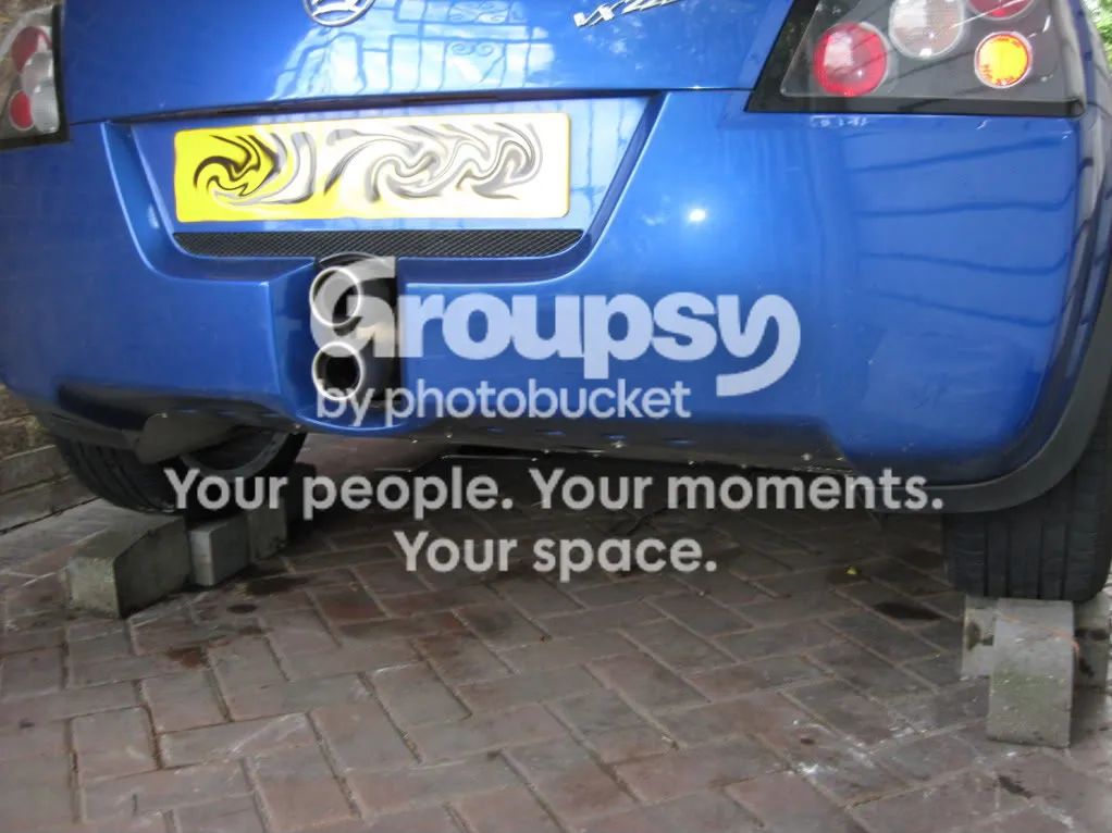 The rear of a blue car with its rear wheels raised on bricks