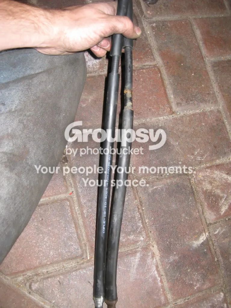 Two black cable outer sheaths held together by a hand, one longer than the other, over paving
