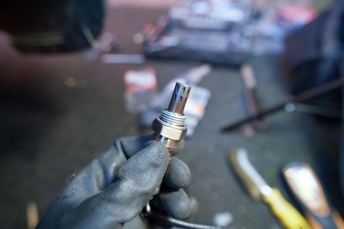 A gloved hand holding the new lambda sensor with its threads showing