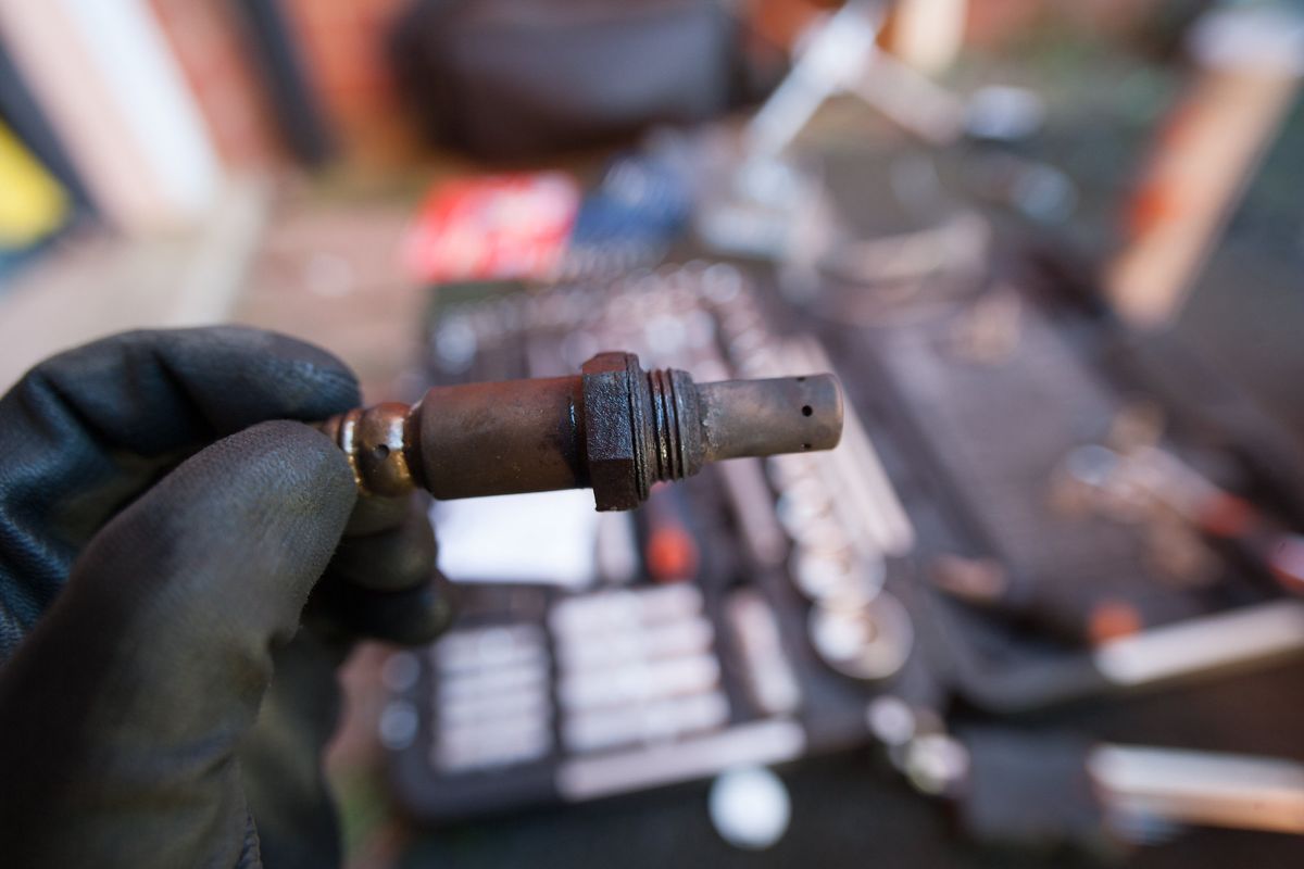A gloved hand holding the old rusty lambda sensor