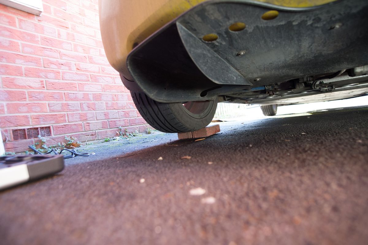 The rear of a yellow car with a rear wheel balanced on bricks, seen from low down