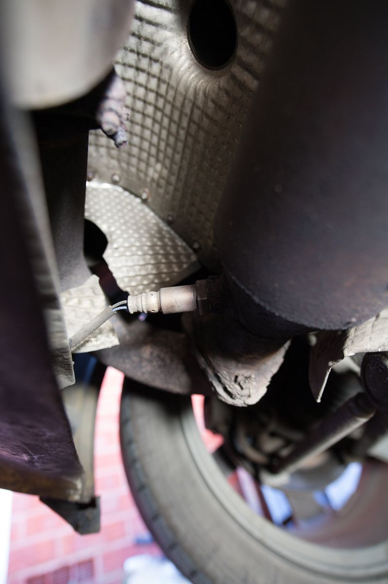 Looking up at the exhaust and heat shield at the rear of the car, with the sensor wire at the bottom