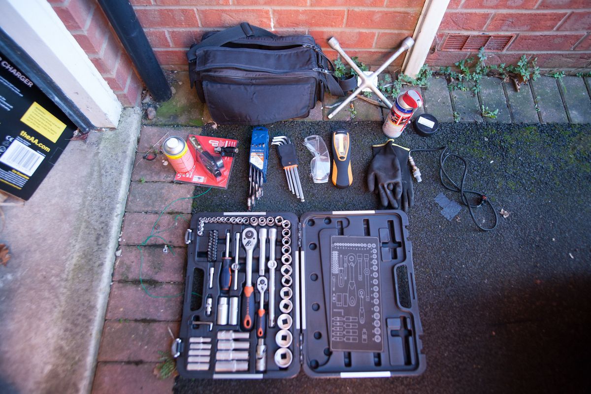 Tools laid out on a driveway: a socket set, Allen keys, spanners, a wheel brace, penetrating oil, safety glasses, gloves and a torch