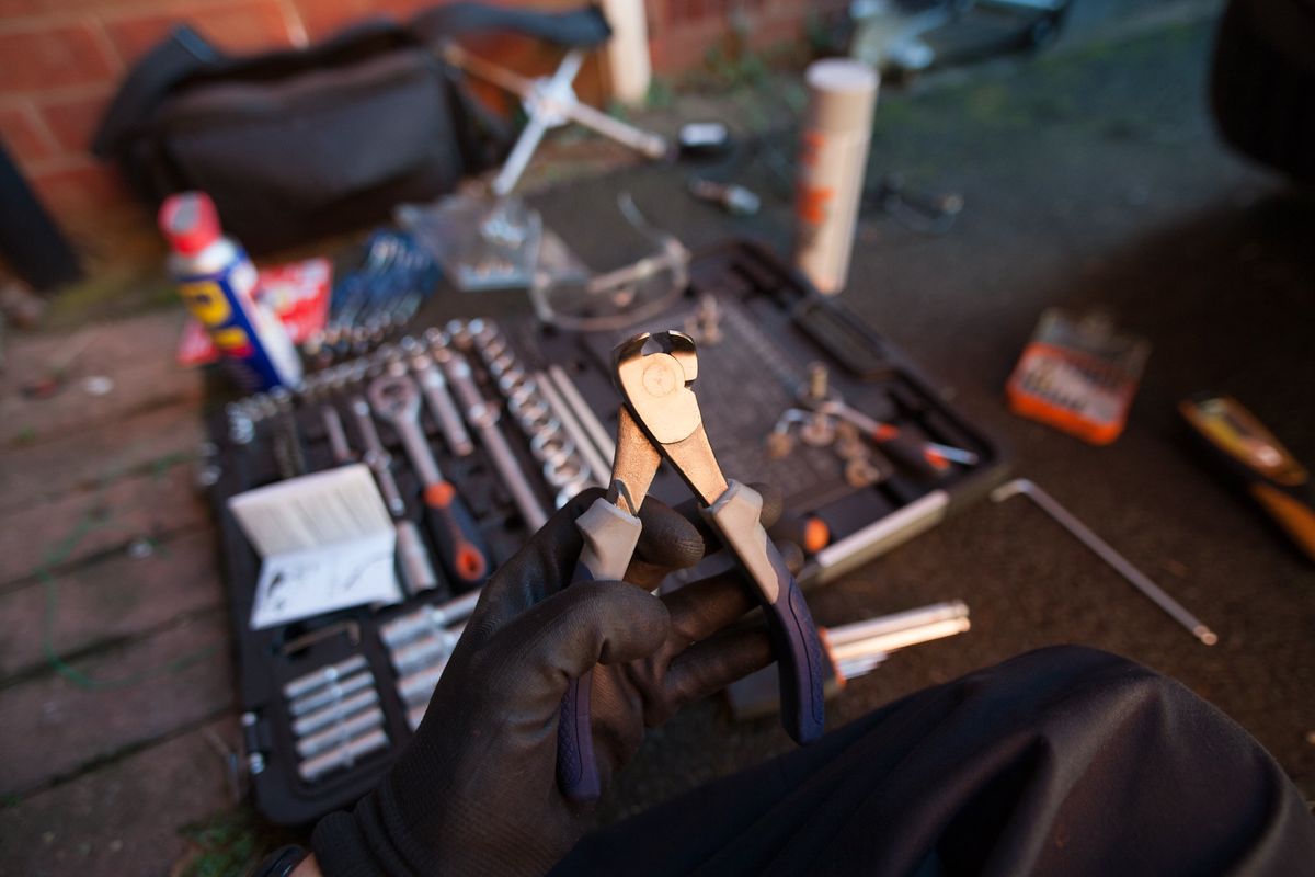 A gloved hand holding wire cutters over a tool set on the ground
