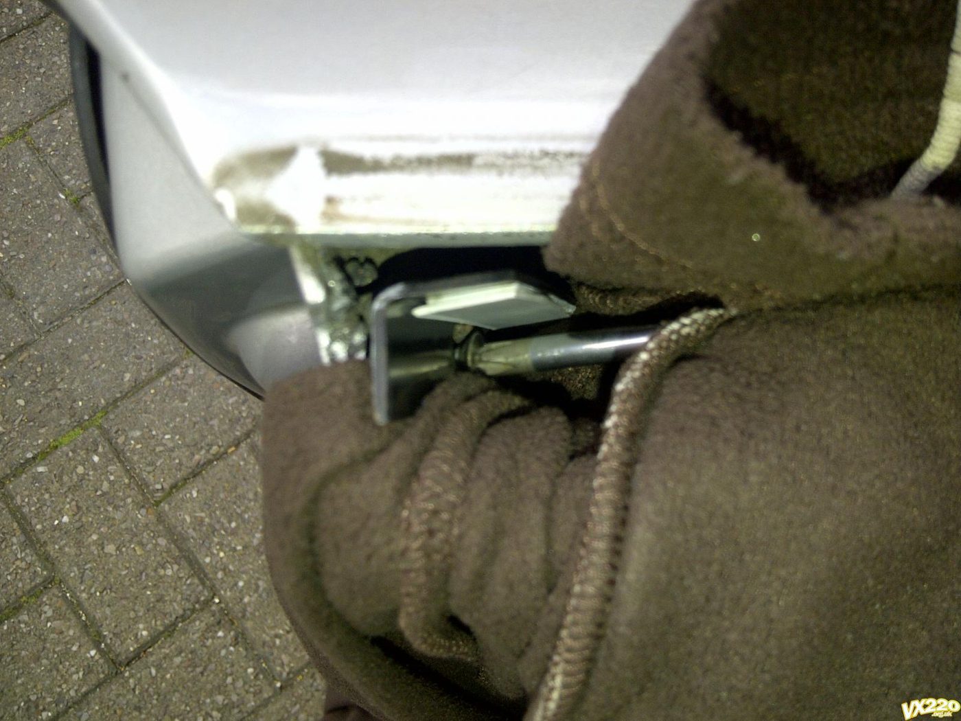 A screwdriver at the top screw hole of the rail in the top of a door, with a brown fleece jumper pushed in underneath