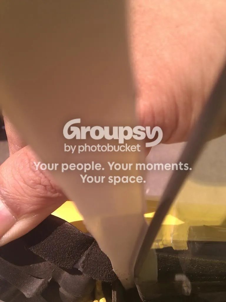 A hand holding a long strip of pale backing paper beside the window glass, with the door seal pulled back below