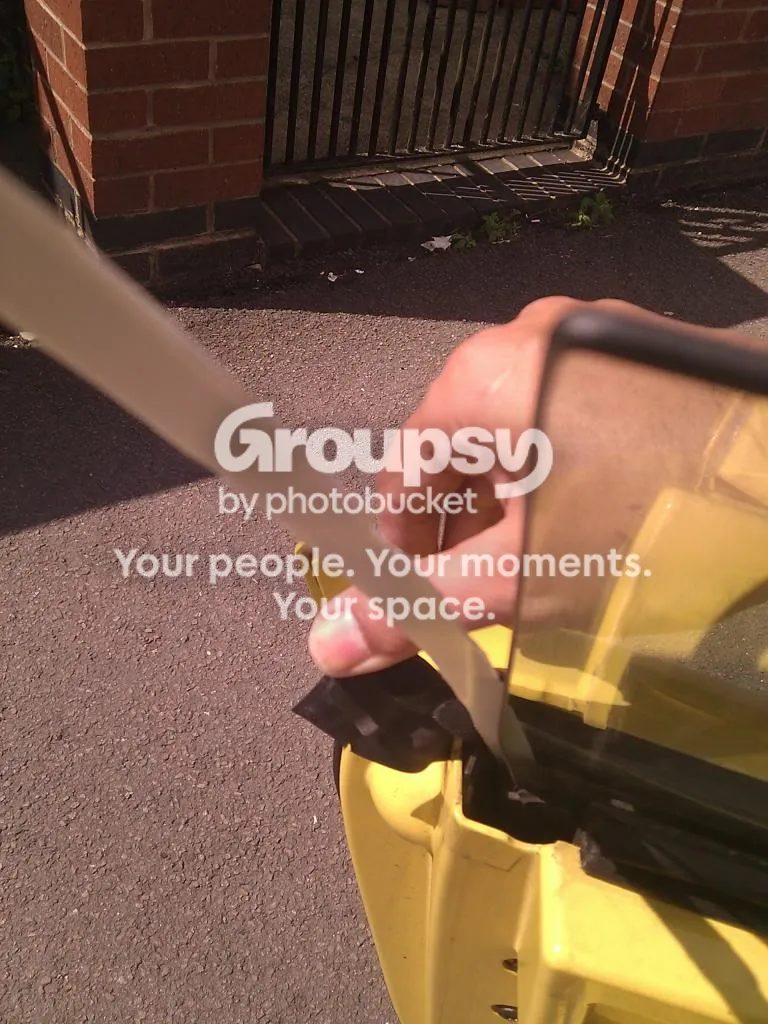A hand pulling the backing off a strip at the edge of a window in a yellow door, with the seal folded back