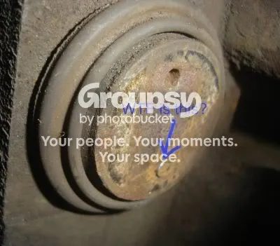 A rusty piston face with a metal blockage over one of the turning holes and an arrow pointing at it