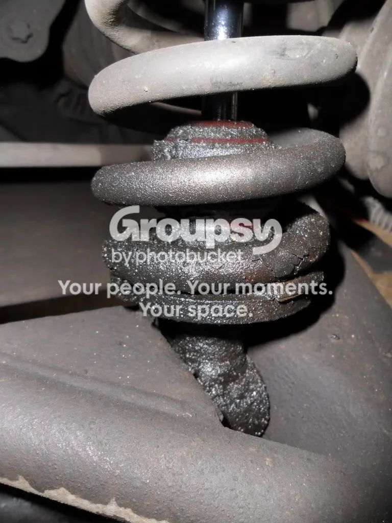 A rear shock with a coil spring and a cracked, crumbling black rubber bump stop and spring seat