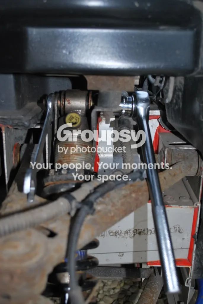 A ratchet and a spanner on the nut and bolt head of the front shock top mount