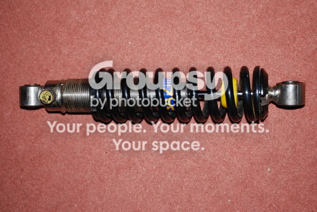An old standard shock with black spring and yellow bump stop lying on a red cloth
