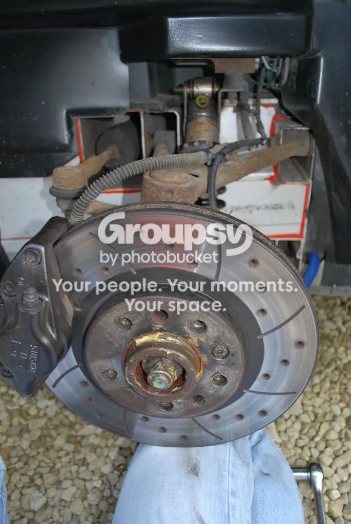A drilled and grooved brake disc on the hub with a knee in jeans pressed under it to support it