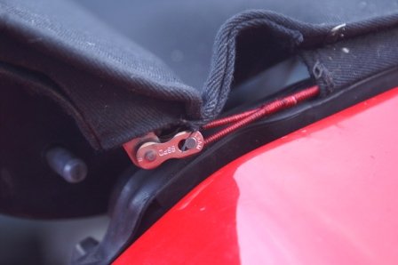 The fabric hood edge folded back to show the chain link and red string between the hood and the red bodywork