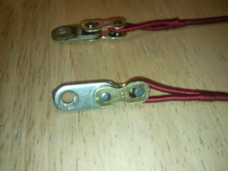 Close-up of two silver-and-gold chain split links joining the plates to red whipped string loops