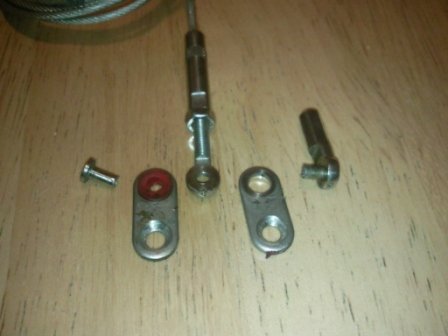 The parts of an old soft top cable laid on a wooden table: two countersunk end plates, a pin, the threaded adjuster and the fixed cable crimp