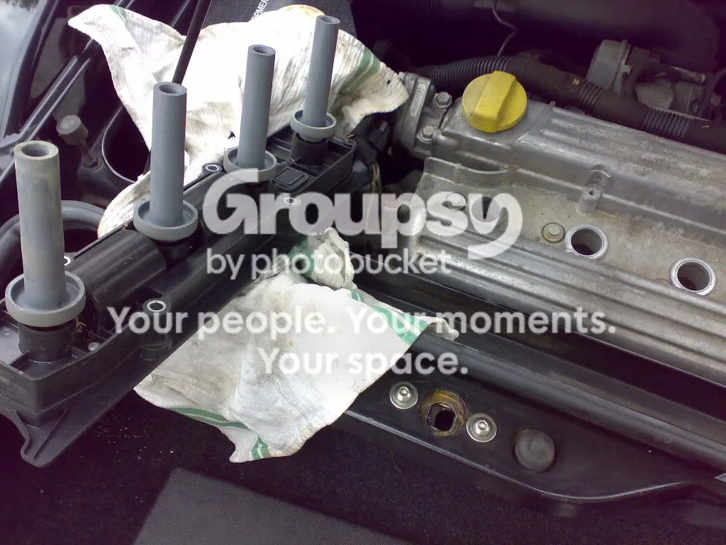 The coil pack lifted off and resting beside the engine, with four grey boots standing up from it