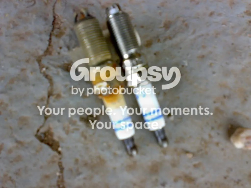 A stained old spark plug lying next to a new one