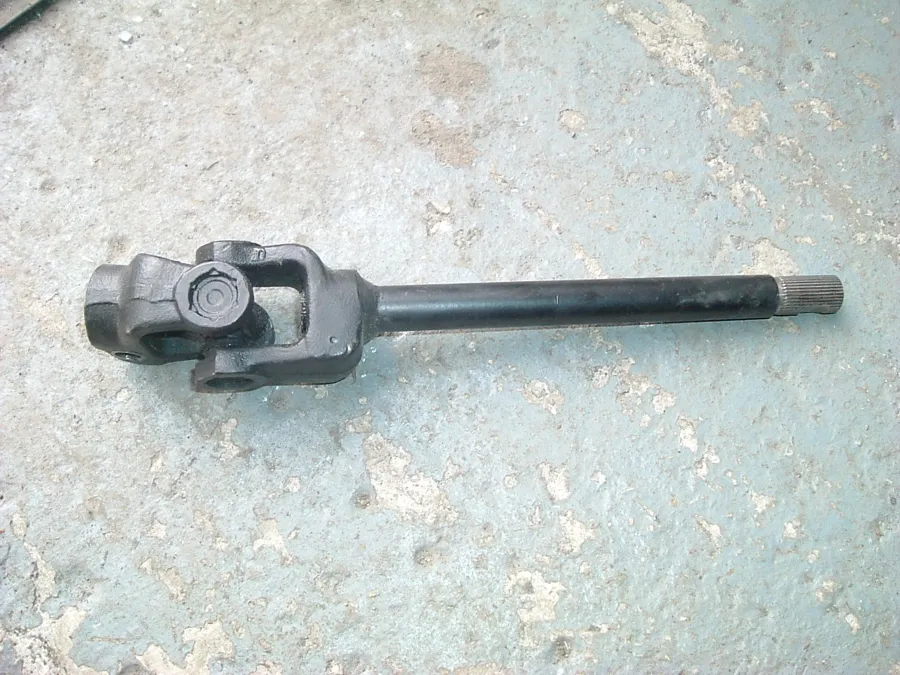 A universal joint with a long splined shaft welded to it, lying on a concrete floor