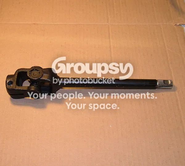 A black intermediate steering shaft with a universal joint at one end lying on cardboard