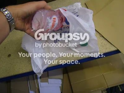 A hand squeezing washing-up liquid into a plastic carrier bag on a workbench