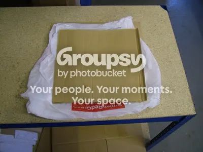 A carrier bag folded round a square of cardboard on a workbench