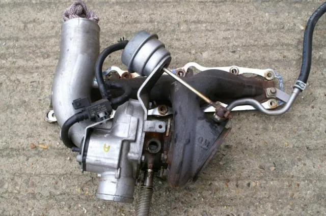 The standard turbo and manifold removed and lying on concrete, with the actuator and oil drain pipe visible