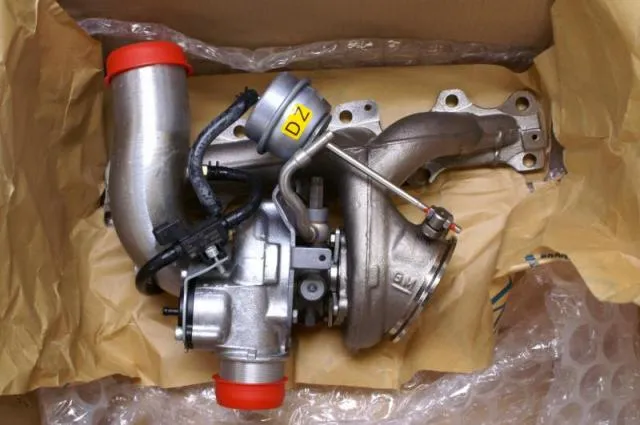 A turbo and cast manifold in a cardboard box with a red cap on the outlet and a yellow Z marking