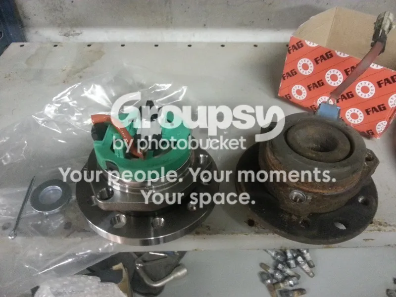 A new FAG hub bearing unit with its sensor, split pin and washer on the left, and an old rusted hub on the right in front of a red FAG box