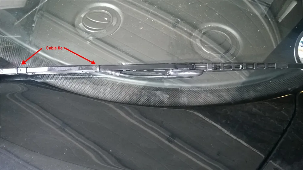 A wiper blade with a spray bar, with cable ties marked in red along the tube that runs up the arm