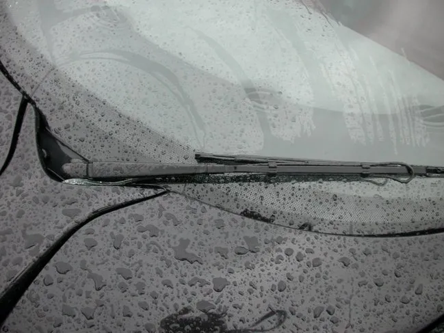 A wiper arm on a wet windscreen with a thin black spray bar running along it